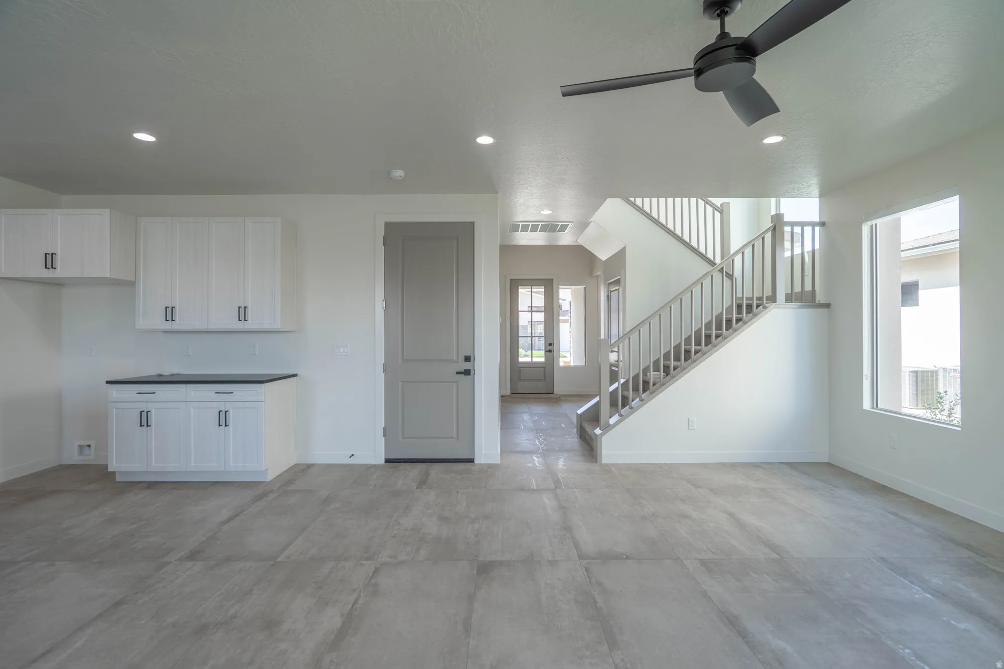 Contemporary interior with large format tile flooring, built-in white cabinetry with dark hardware, a gray paneled door, and a staircase with a wood-finish railing