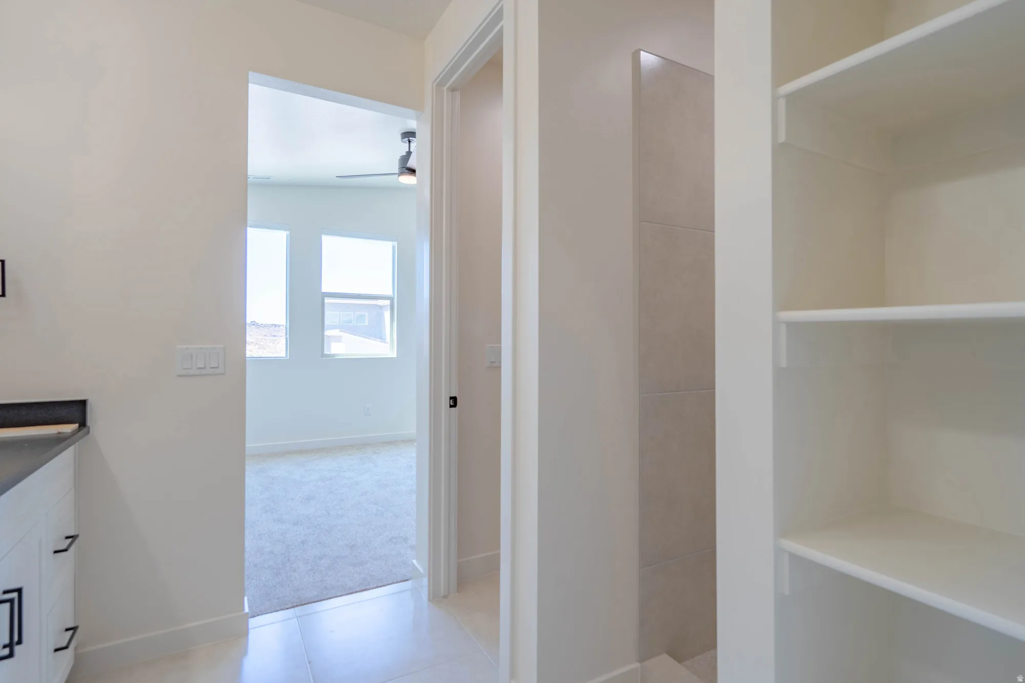 Built-in shelving, tiled shower enclosure, white vanity with dark countertop, white walls, and light-toned flooring