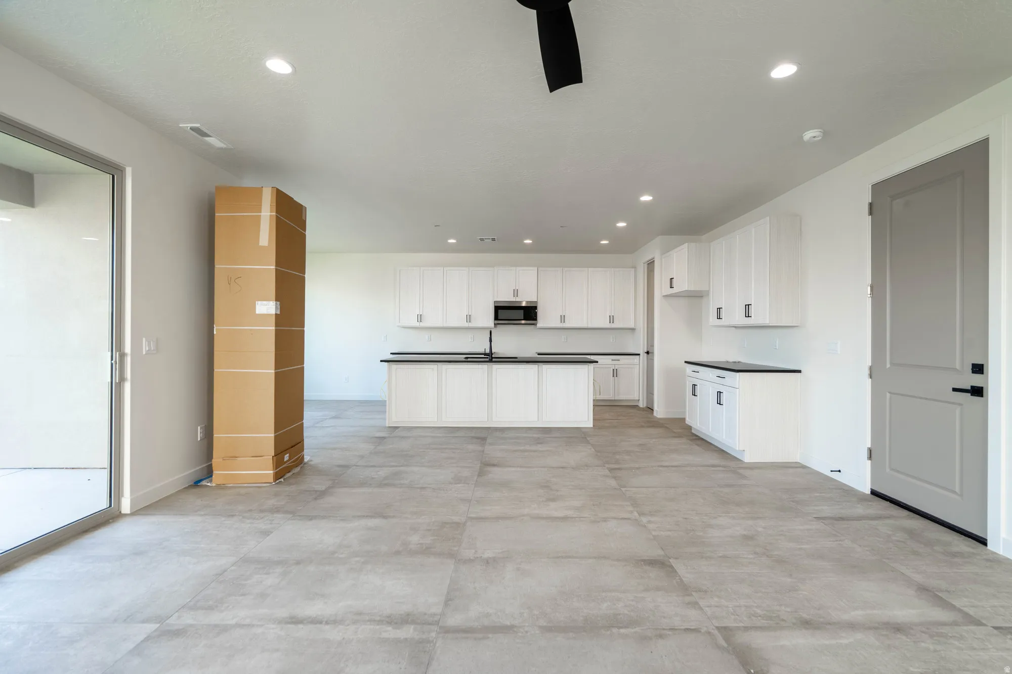 Spacious living area with large format tile flooring, recessed lighting, and a modern kitchen featuring white cabinetry and dark countertops
