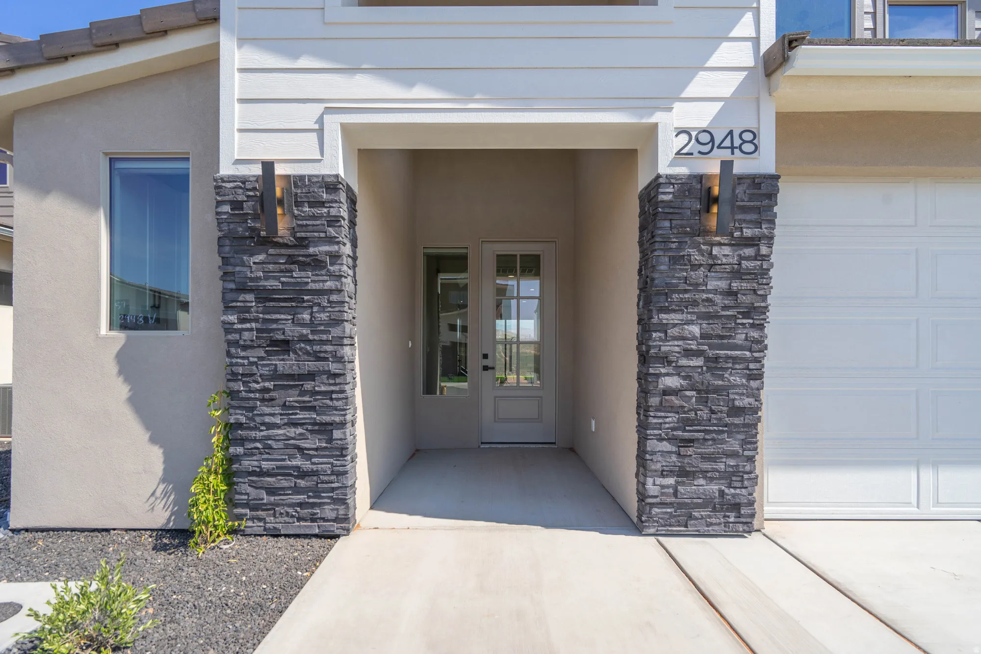Stucco exterior with stacked stone accents, covered entry, front door with glass panels, and an attached garage