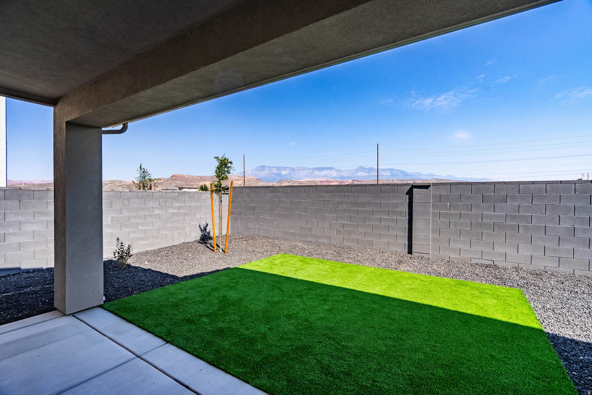 Covered patio with a concrete slab, artificial turf, gravel landscaping, and block walls