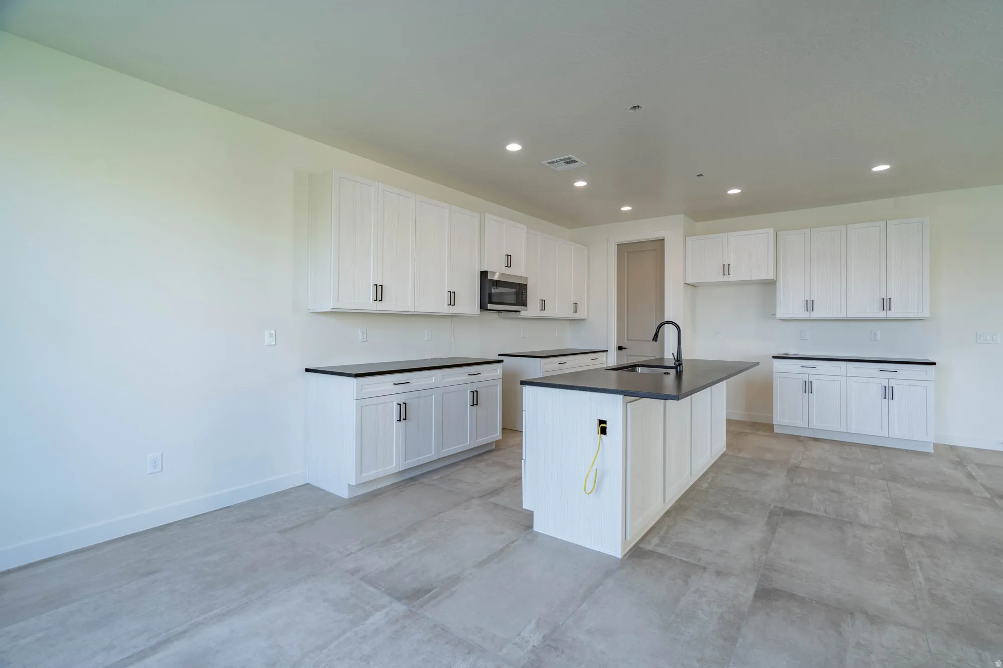 Kitchen featuring extensive white cabinetry, dark countertops, a central island with a built-in sink, and tile flooring