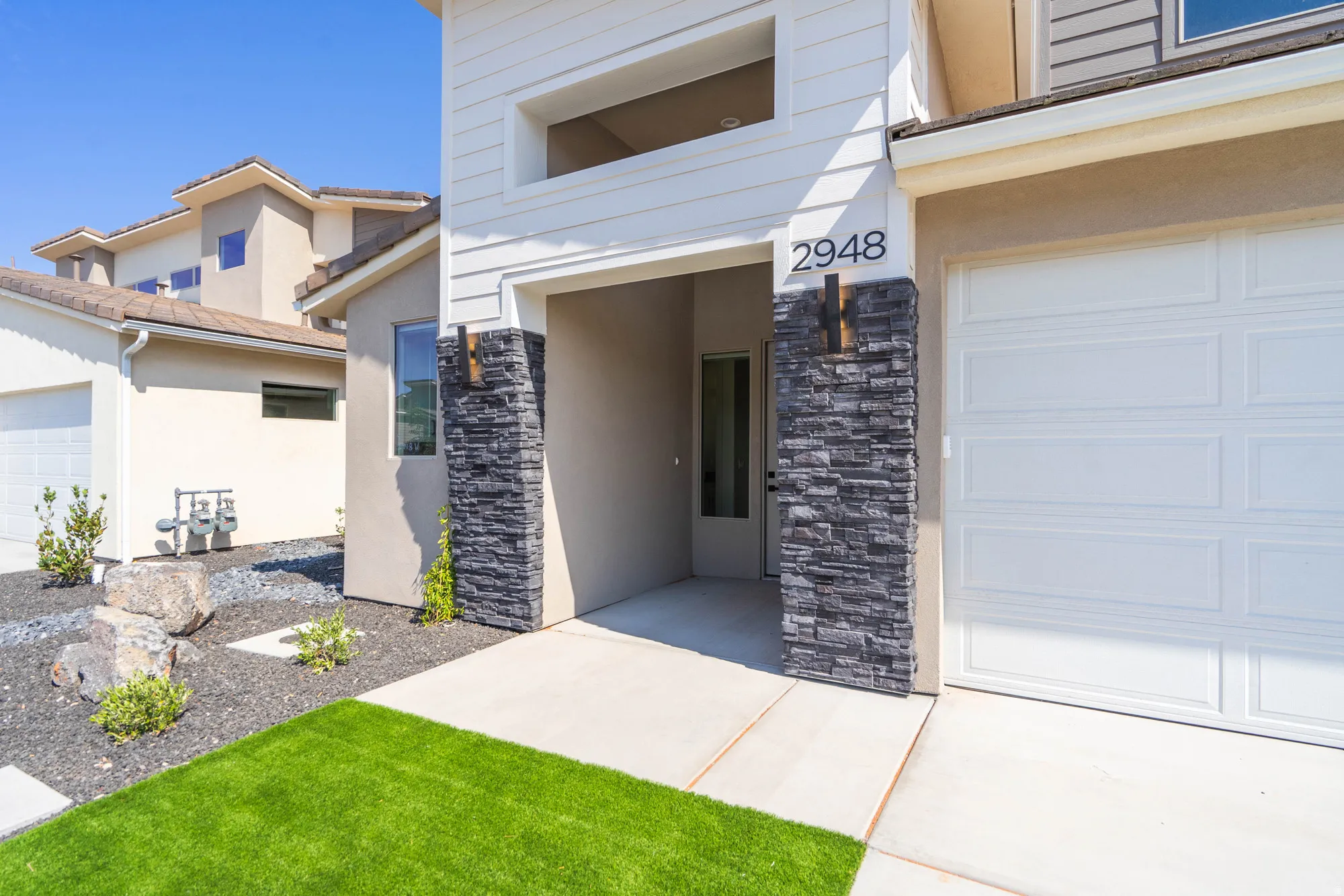 Entryway featuring stacked stone accents, covered porch, and a panel garage door