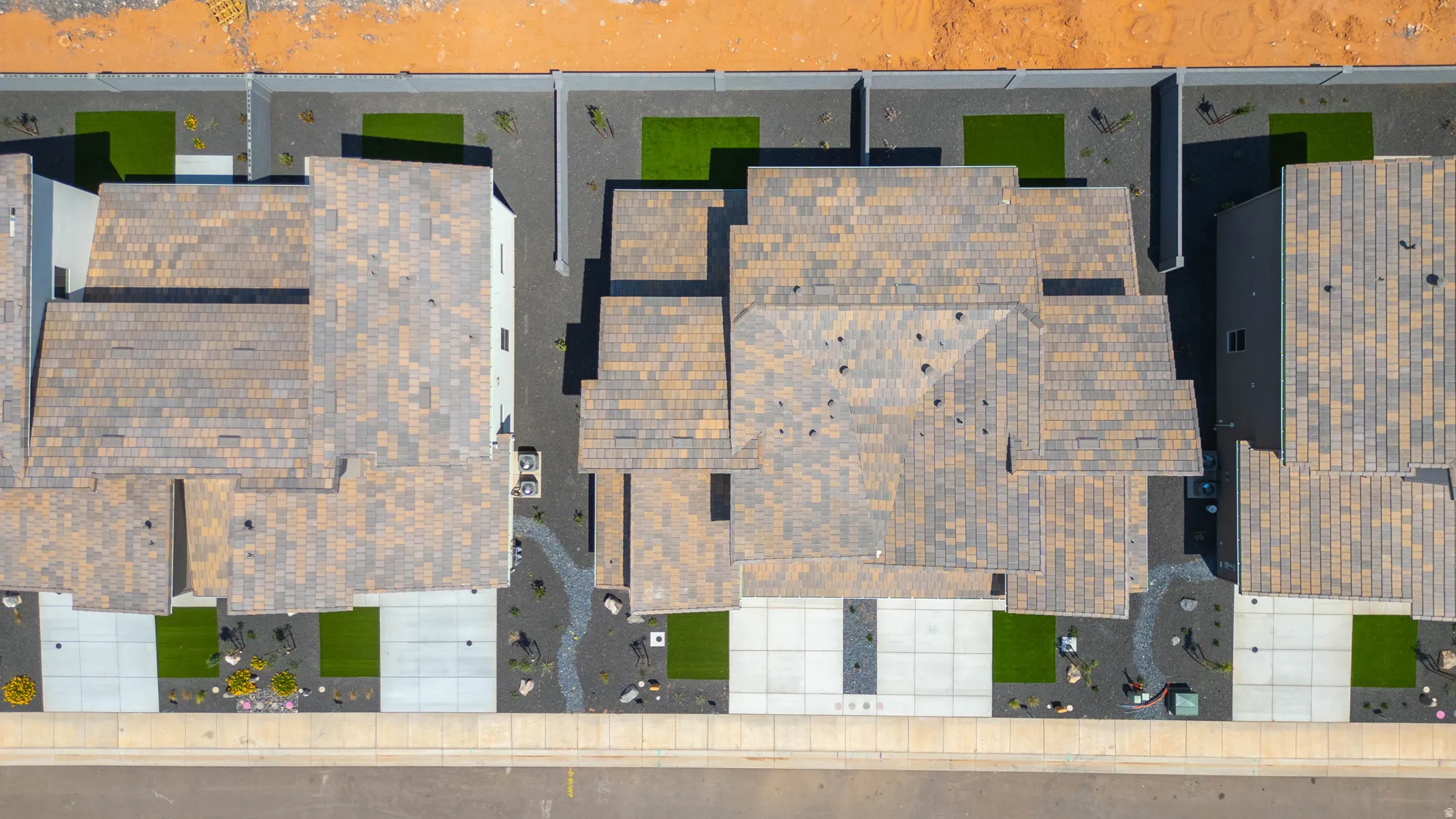 Pitched roof with multi-tone shingles, concrete driveway, front yard landscaping with artificial turf and decorative rock, paved walkway, and a concrete paver patio