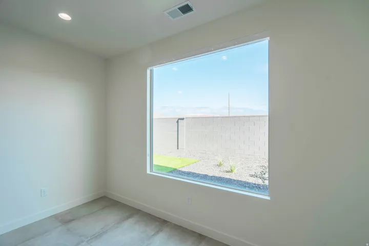 Bright corner bedroom showcasing expansive windows framing outdoor landscape, polished concrete flooring, and recessed ceiling lighting