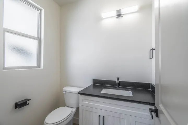 Modern bathroom featuring a white cabinetry vanity with a black countertop and integrated rectangular sink, chrome faucet, and polished nickel hardware