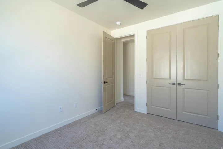 Neutral tone wall color with carpeted flooring, featuring a ceiling fan, light-toned interior doors, and a double-door closet