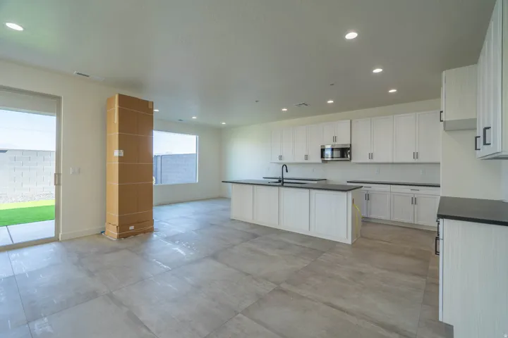 Spacious open-concept living area featuring large format tile flooring, a modern kitchen with white cabinetry, dark countertops, and a built-in microwave