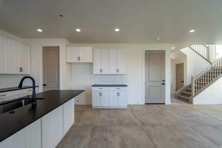 Kitchen island with a dark countertop and undermount sink, white cabinetry with dark hardware, recessed lighting, and wood-look flooring