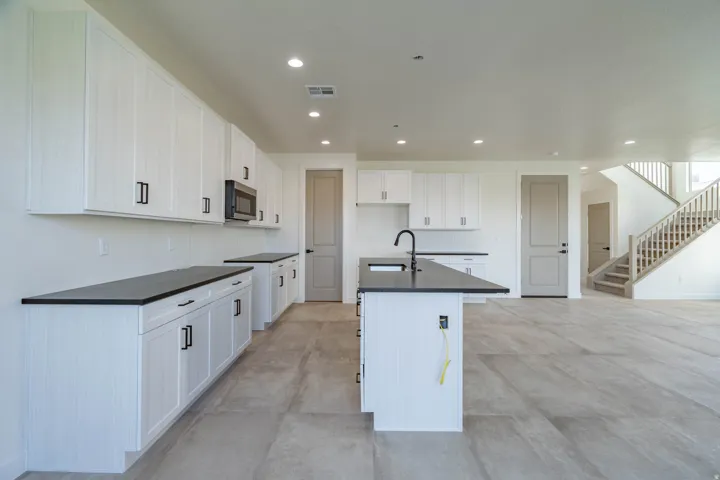 Kitchen featuring white cabinetry, dark countertops, a built-in microwave, and a central island with a sink