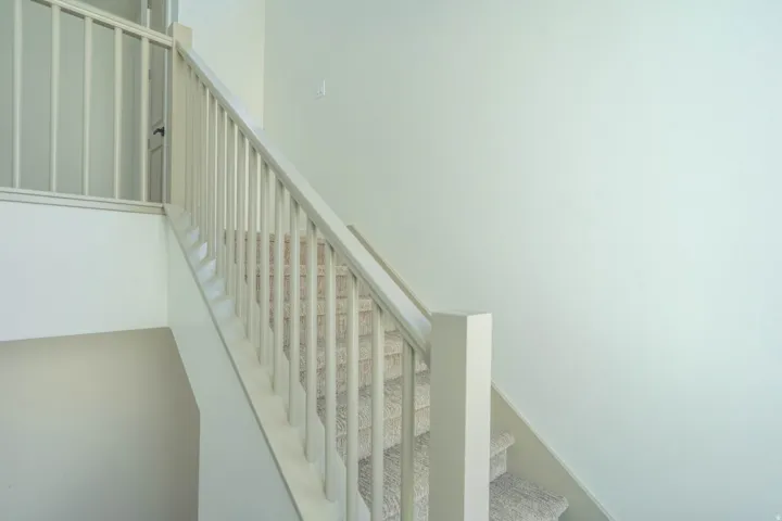 Carpeted staircase featuring a light-toned wooden banister and painted risers