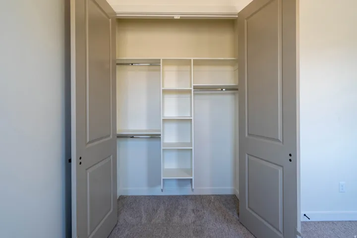 Built-in closet organization system with shelving, dual closet rods, panel doors, and neutral carpeting