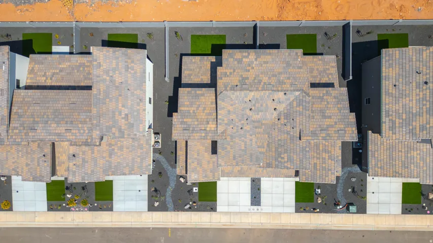 Pitched roof with multi-tone shingles, concrete driveway, front yard landscaping with artificial turf and decorative rock, paved walkway, and a concrete paver patio