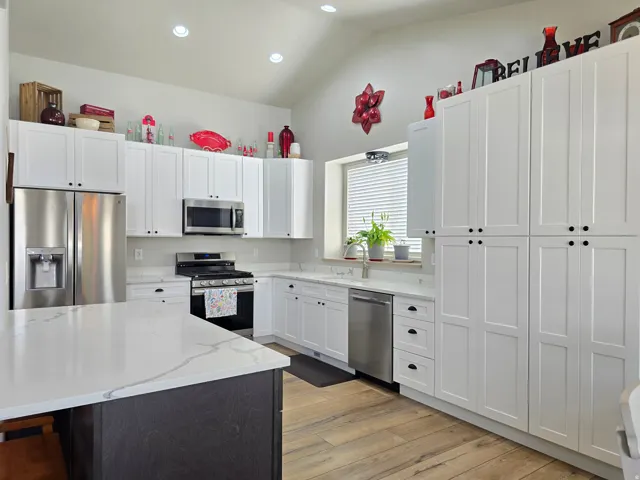 Kitchen with vaulted ceiling, white shaker cabinetry, stainless steel appliances, white countertops, and wood-finish flooring
