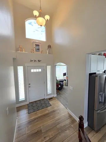 Vaulted ceiling with an arched window, wood-finish flooring, recessed niche, and a contemporary chandelier