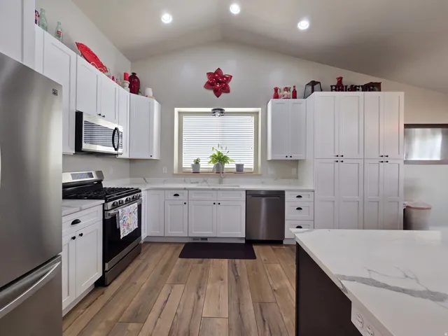 Kitchen featuring white cabinetry, stainless steel appliances, wood-finish flooring, light-toned countertops, and a vaulted ceiling
