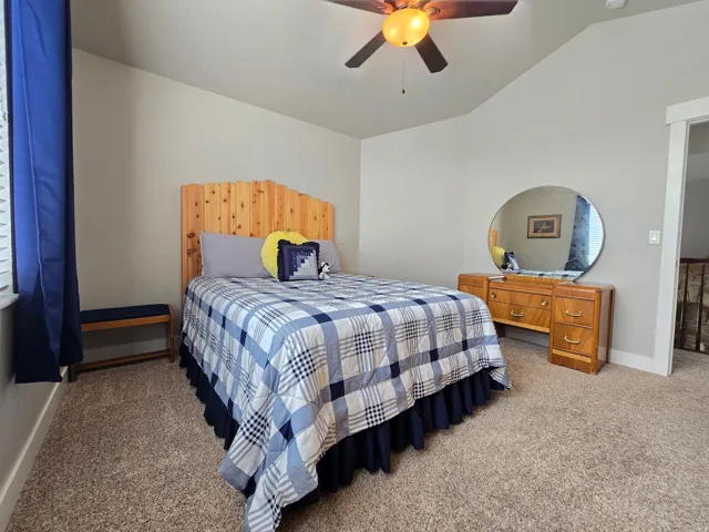Carpeted flooring, vaulted ceiling, ceiling fan with integrated lighting, natural wood headboard