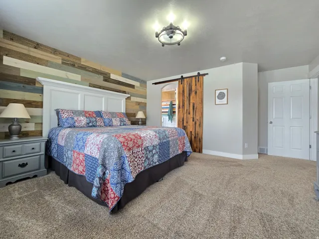 Carpet flooring, wood-paneled accent wall, white paneled headboard, wood barn door, and a flush mount light fixture
