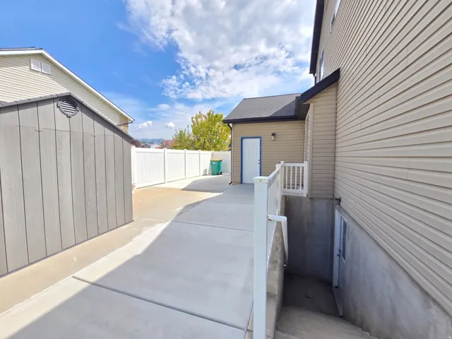 Concrete side yard with a white privacy fence, a detached shed, exterior lighting, and a lower-level entry