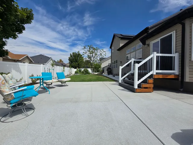 Expansive concrete patio with a manicured lawn, white vinyl fencing, and a built-in deck with white railings