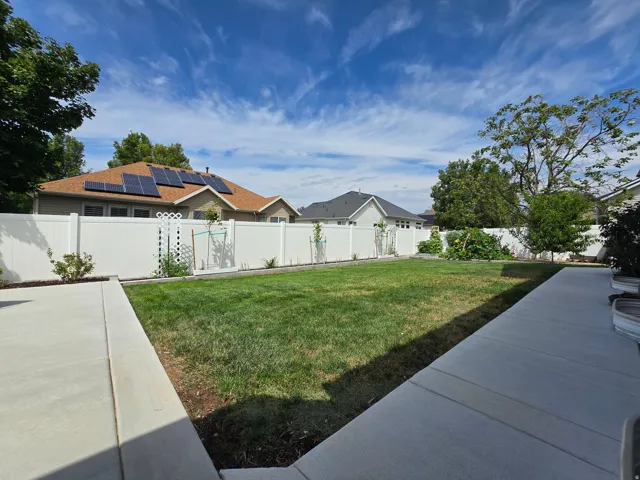 Expansive backyard featuring a manicured lawn bordered by mature landscaping and a modern composite patio