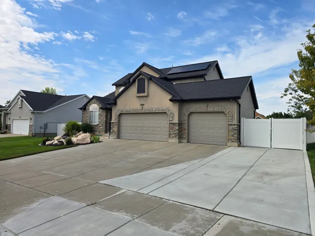 Exterior featuring stucco and stone facade, dual garage doors, solar panels, and a white vinyl fence