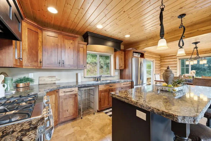 Gourmet kitchen featuring wood-finish cabinetry, granite countertops, stainless steel appliances, and a wood-paneled ceiling with recessed lighting