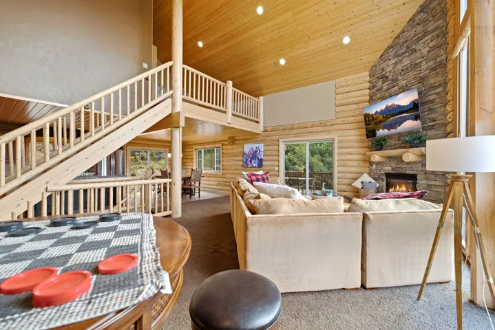 Spacious living area featuring a stone-clad fireplace, wood-finish walls, exposed wood ceiling, and an open loft