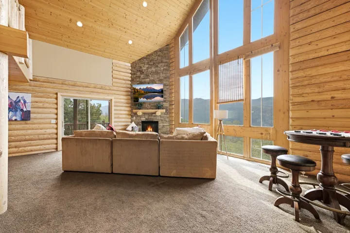 Vaulted wood-paneled ceiling, floor-to-ceiling windows, stone fireplace with mantel, and a sliding glass door