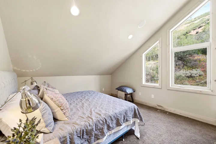 Sloped ceiling with recessed lighting, two large windows, and carpeted flooring