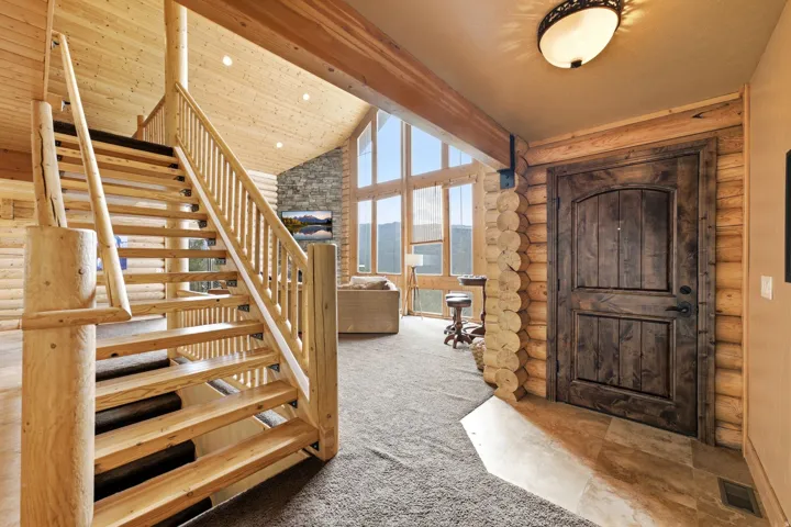 Vaulted wood-paneled ceilings, natural wood staircase, stone accent wall, large picture windows, and a dark wood paneled door