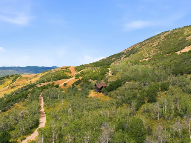 Mountainous terrain with natural landscaping, a winding dirt road, and a single-family residence featuring a brown exterior