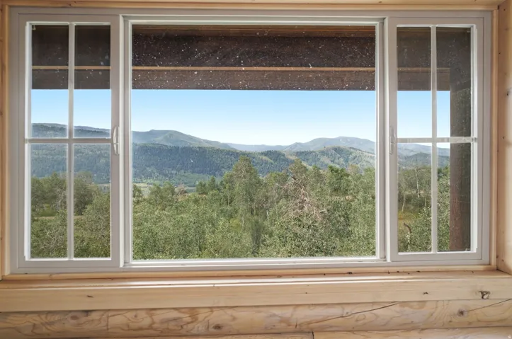 Sliding window with grid inserts, natural wood-finish window frame, and a distant mountainous landscape