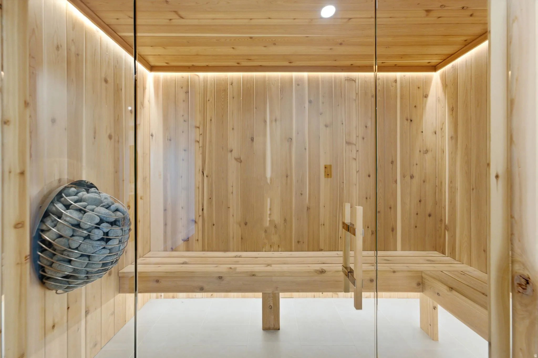 Wood-paneled sauna featuring a glass door, built-in wooden benches, and accent lighting
