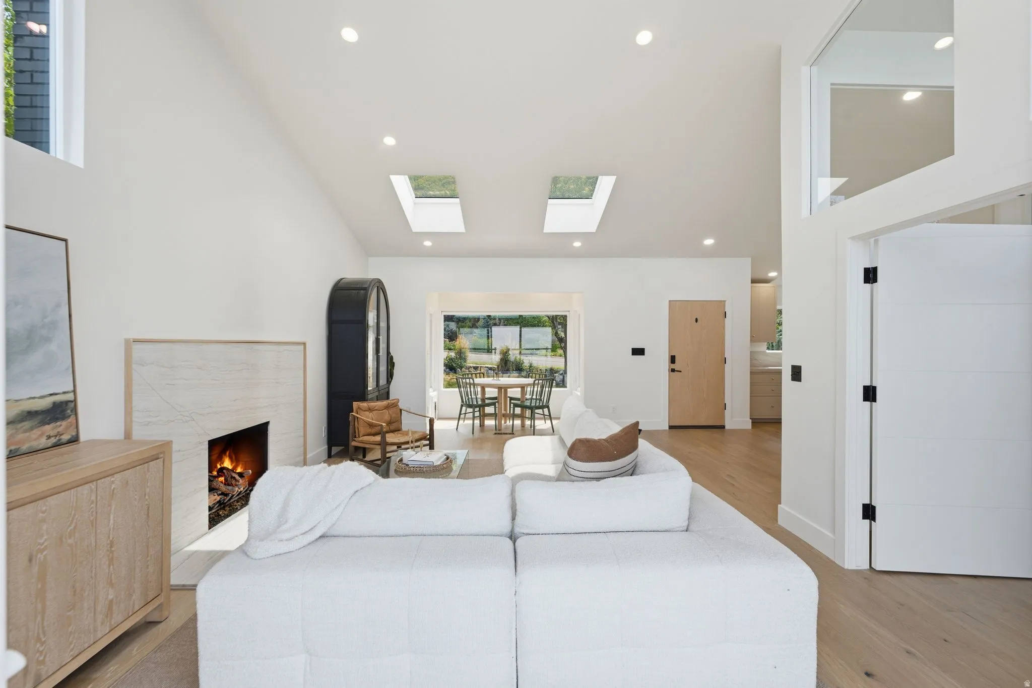 Vaulted ceilings with recessed lighting, two skylights, a fireplace with a stone surround, and wood-finish flooring throughout