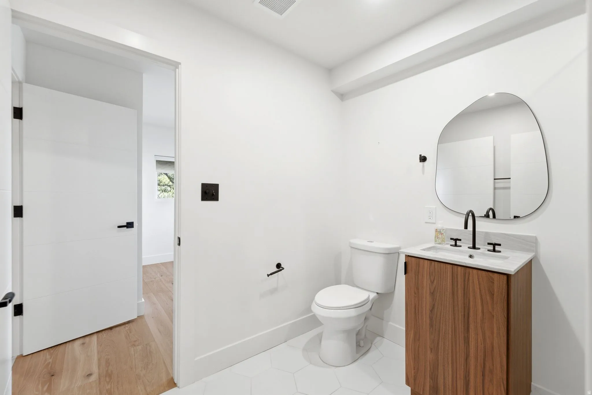 Bathroom featuring a wood-finish vanity with a stone countertop, matte black faucet, and a contemporary mirror