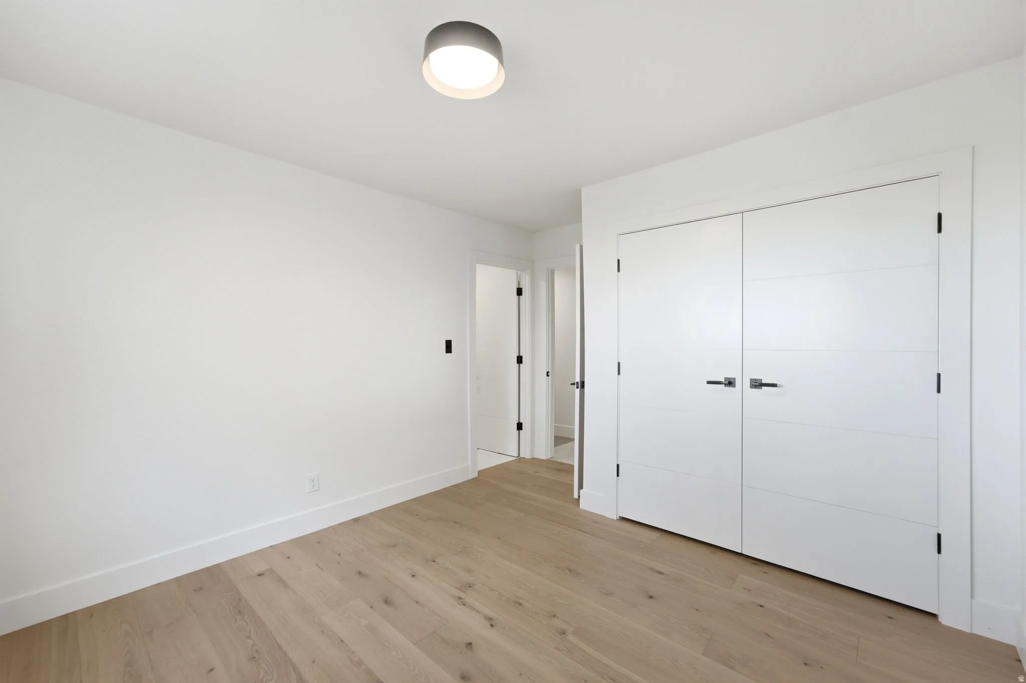 Hardwood-finish flooring, recessed ceiling light, white panel doors with black hardware, white walls, and white trim