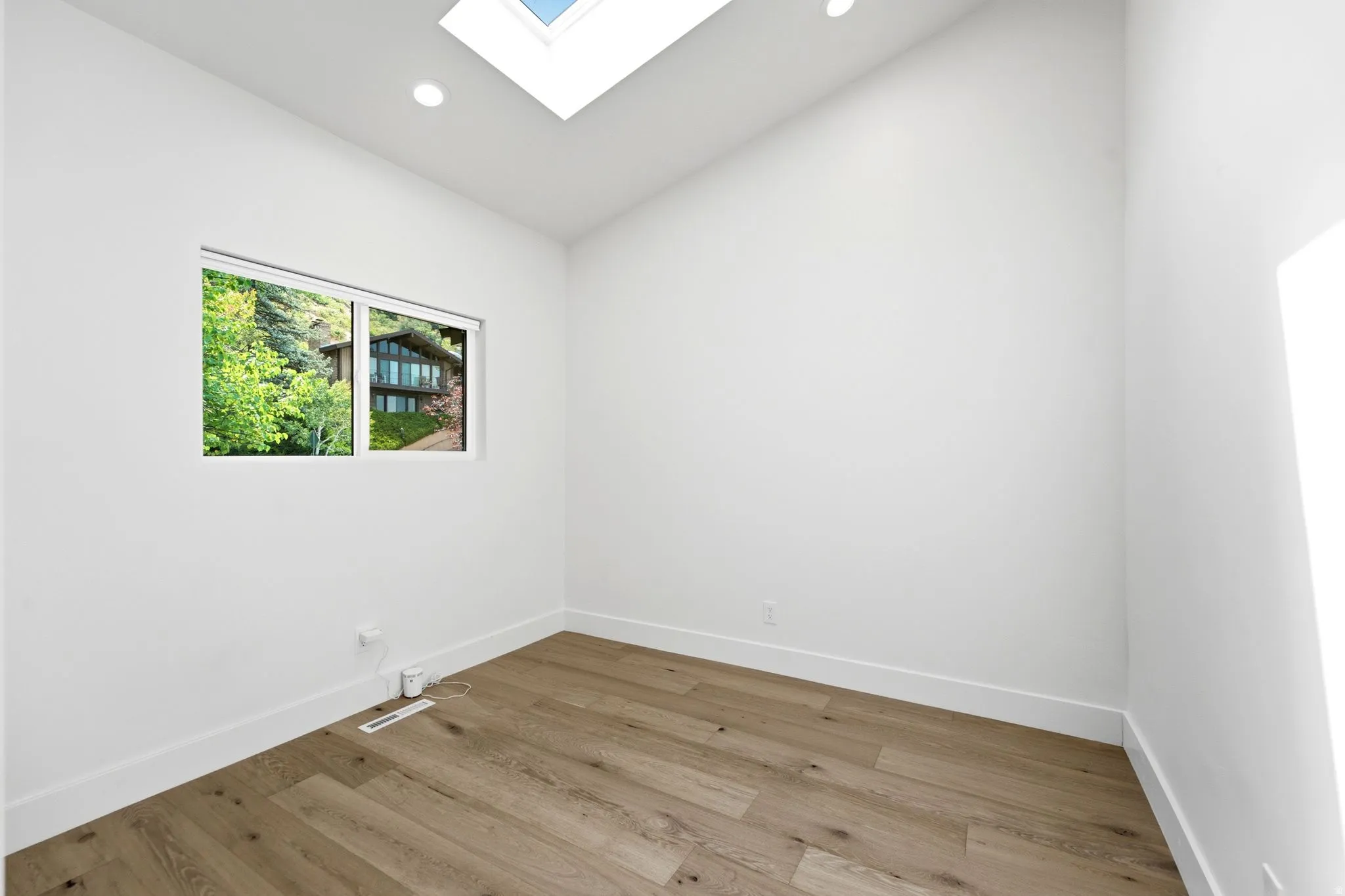 Skylight, recessed lighting, wood-finish flooring, white walls, and a window with exterior foliage