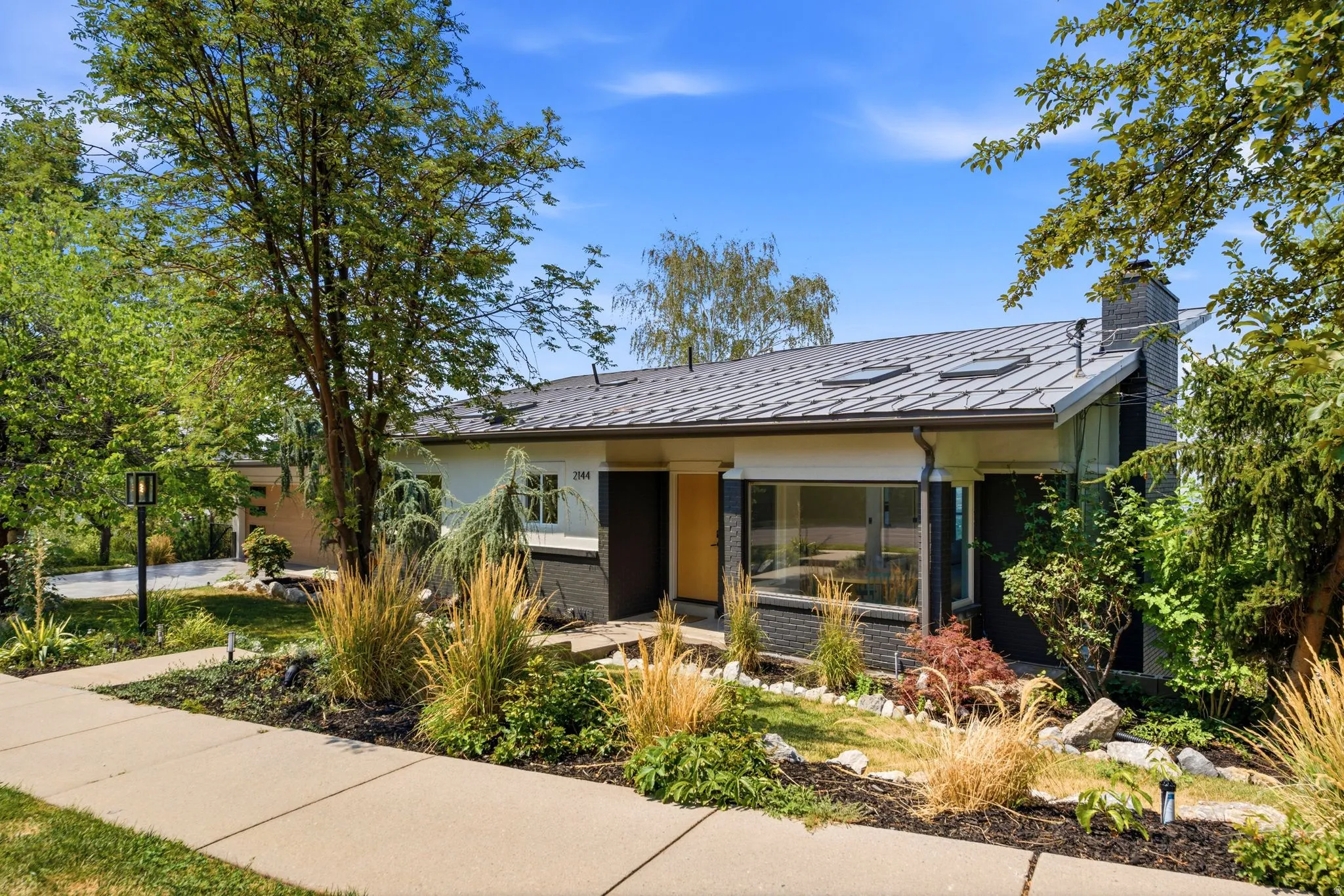 Contemporary exterior with a dark metal roof, multiple skylights, and a prominent brick chimney