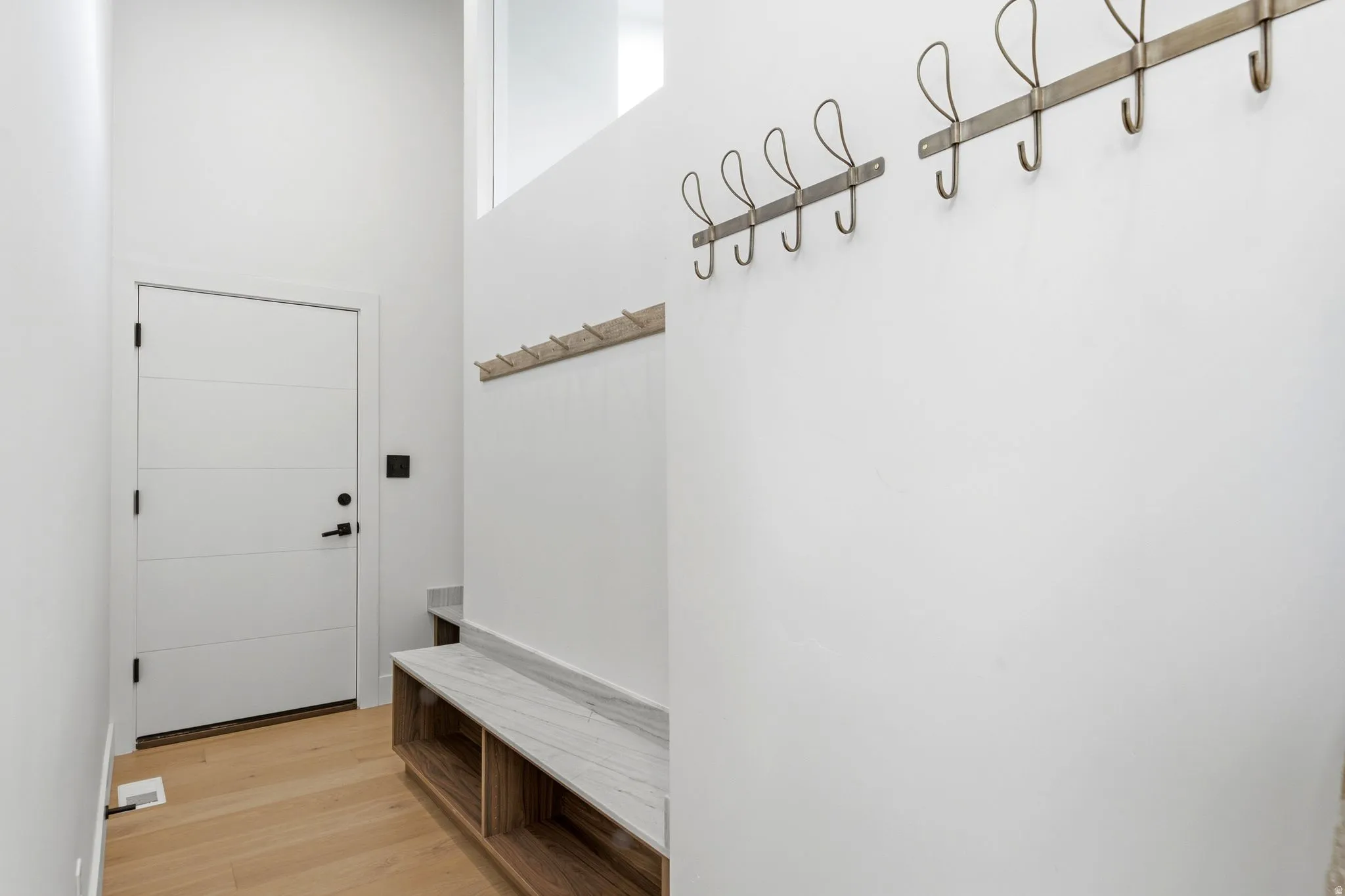 Entryway featuring a modern paneled door, light wood-finish flooring, and a built-in bench with a stone surface