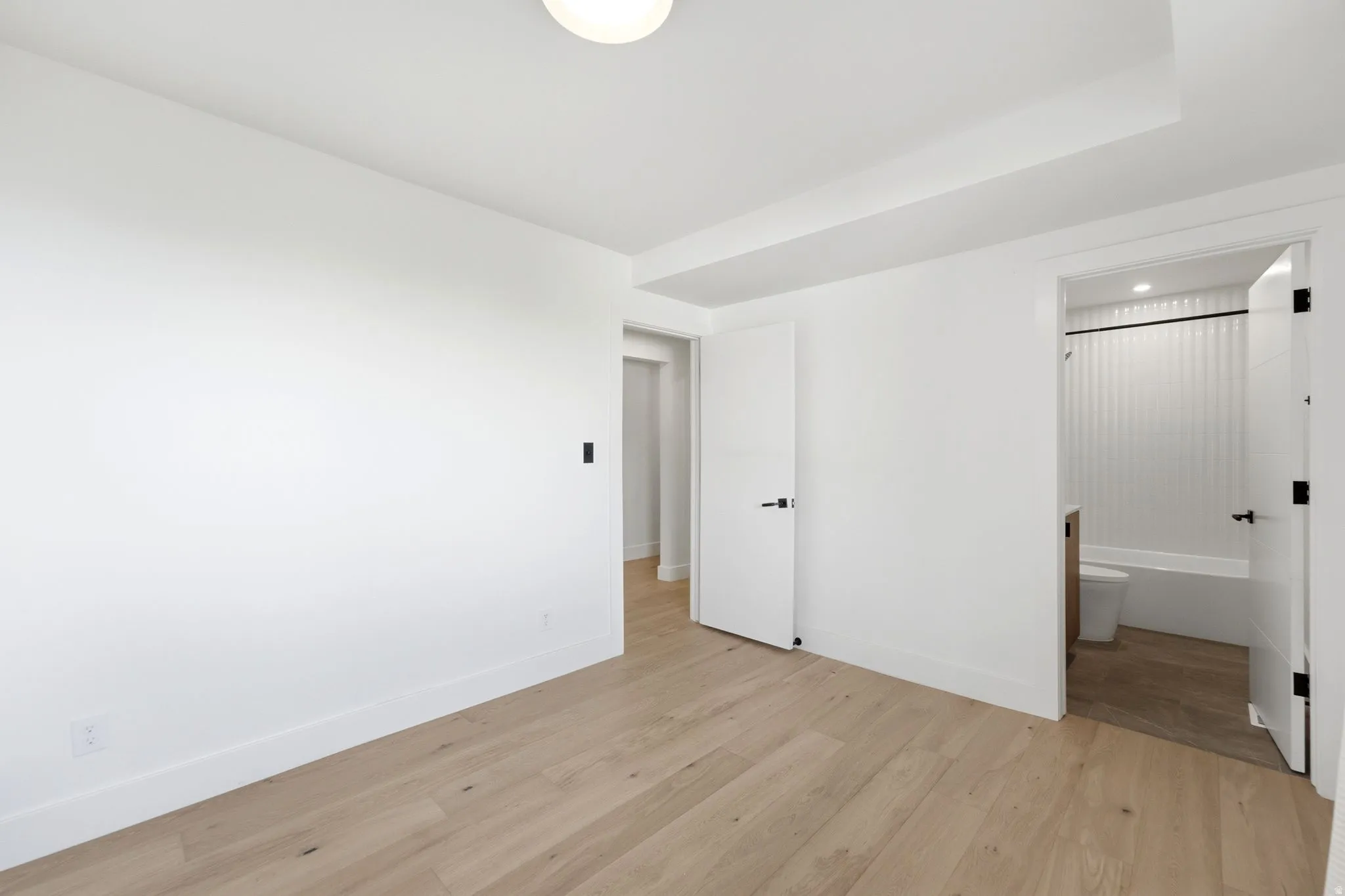 Light wood-finish flooring, white walls, modern interior doors with black hardware, and a ceiling light fixture