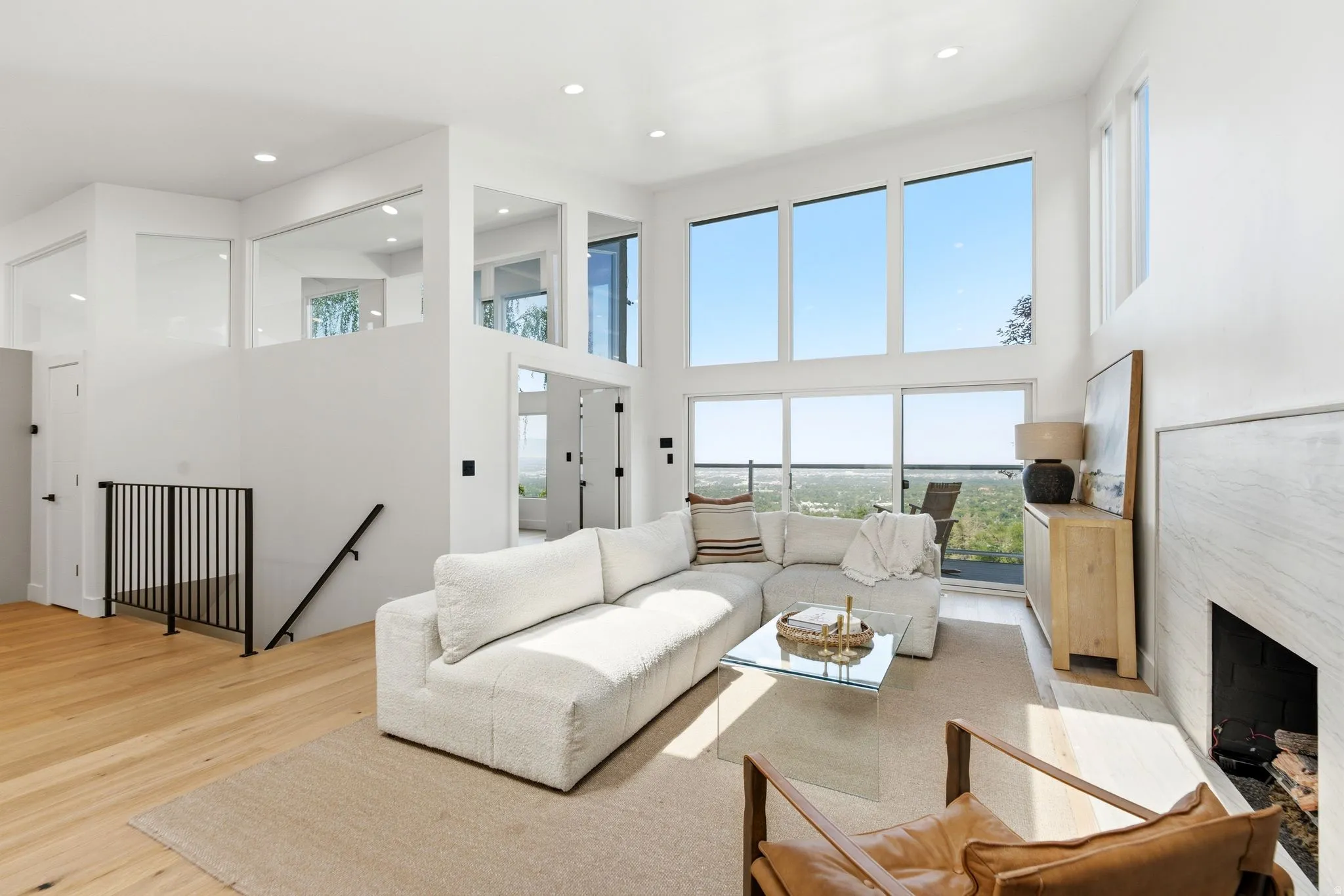 Vaulted ceilings with recessed lighting, expansive floor-to-ceiling windows, wood-finish flooring, a contemporary fireplace, and a black metal staircase railing