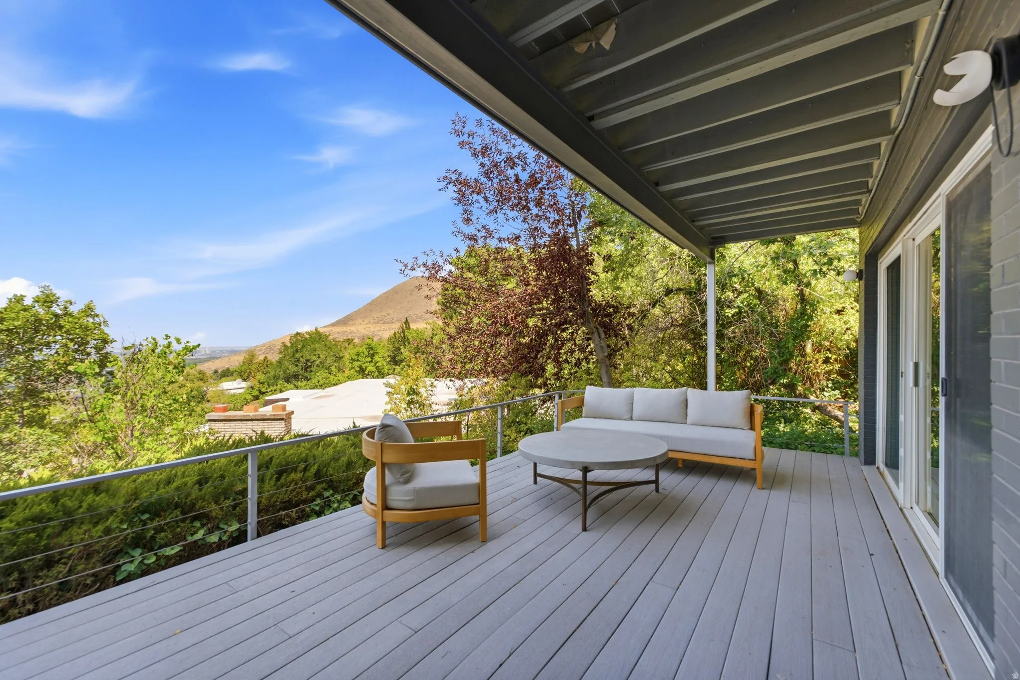 Covered outdoor deck with light gray wood-finish flooring, white sliding glass doors, and a cable railing system