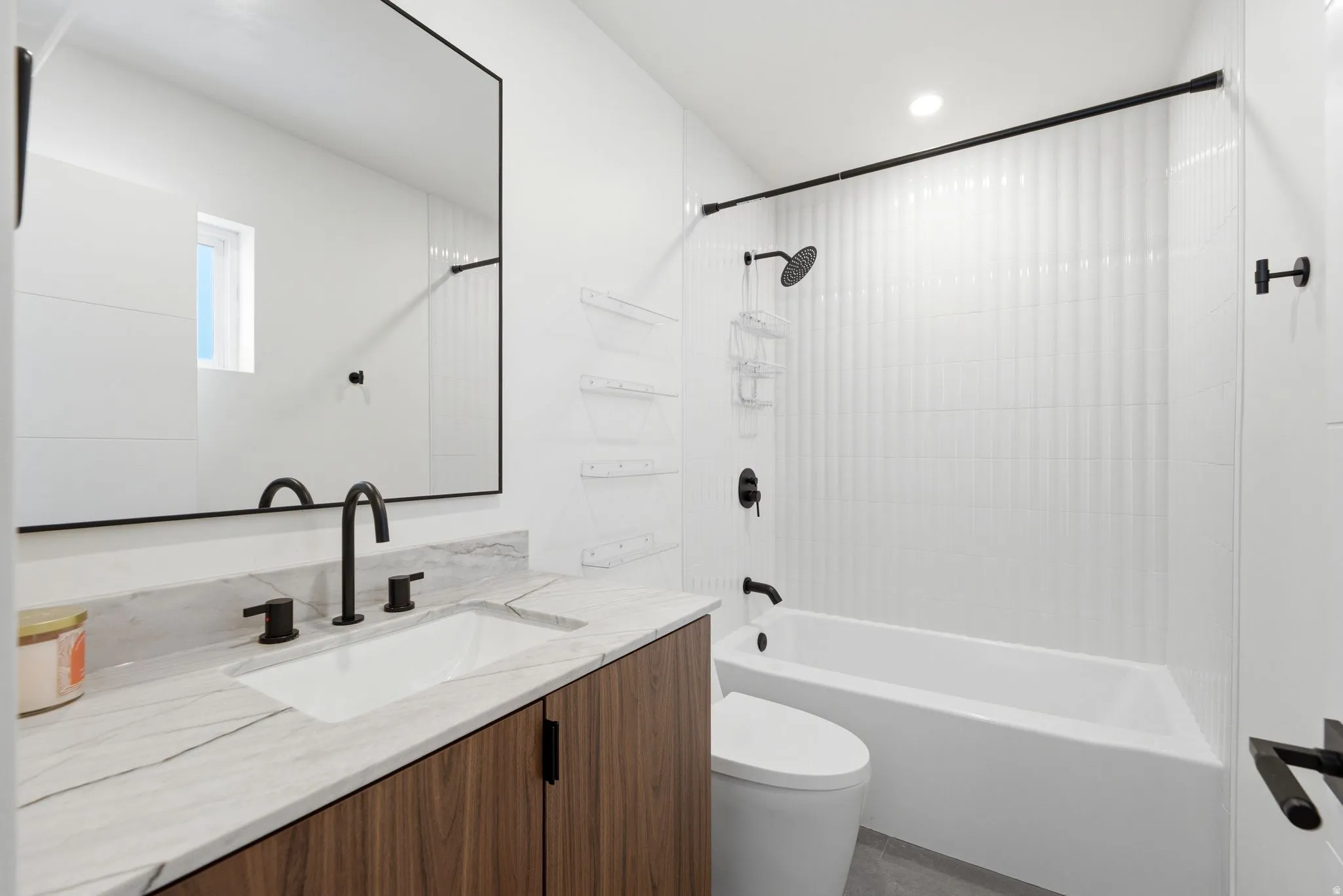 Bathroom featuring a floating wood-finish vanity, undermount sink, stone countertop, matte black fixtures, and a bathtub with vertical tiled surround