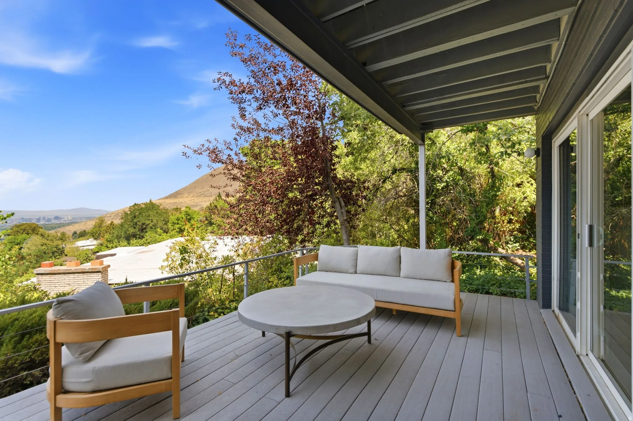 Covered outdoor deck with light gray decking, metal railing, and a sliding glass door