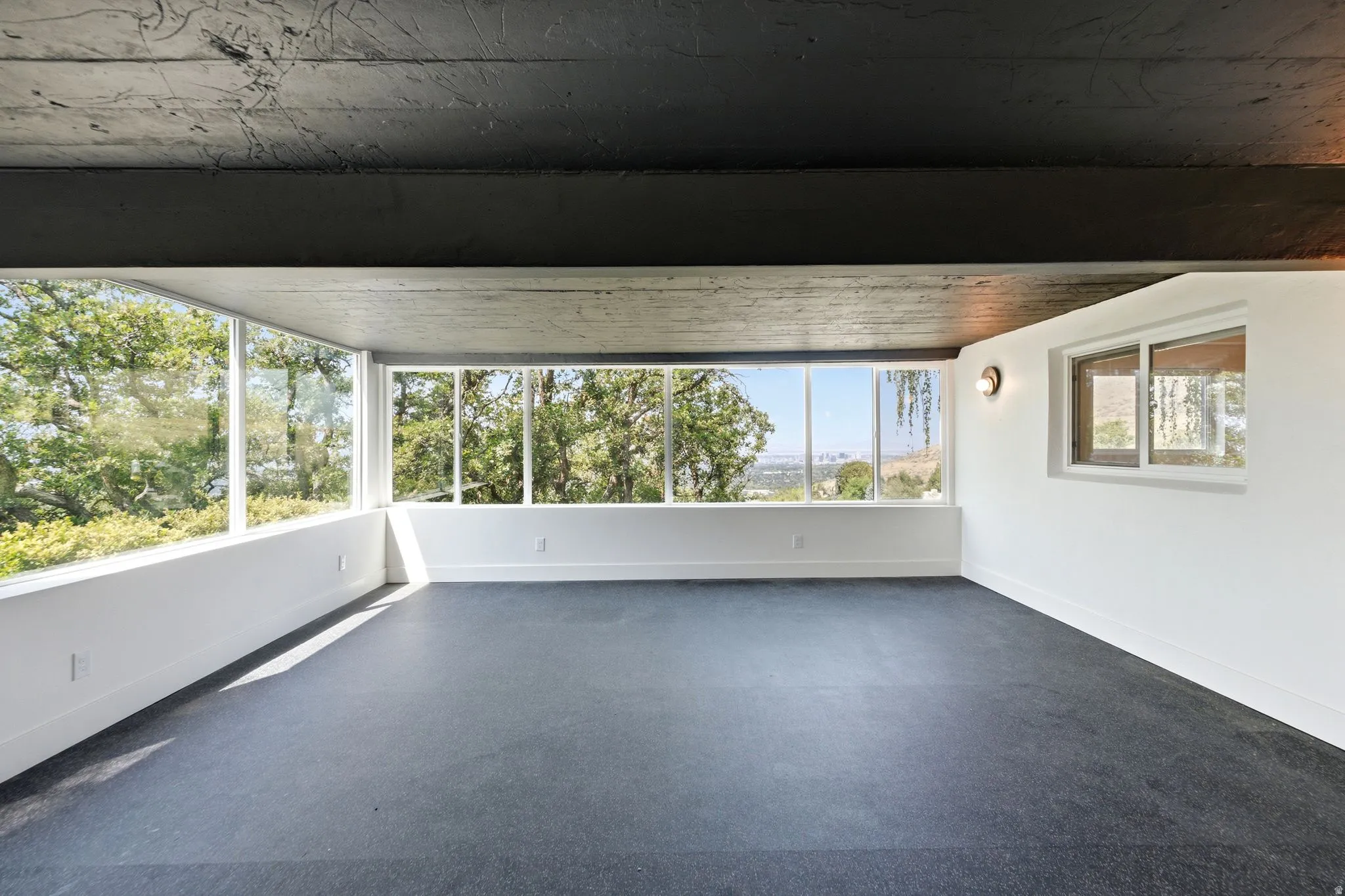 Expansive windows providing abundant natural light, dark flooring, white walls, and a visible ceiling beam
