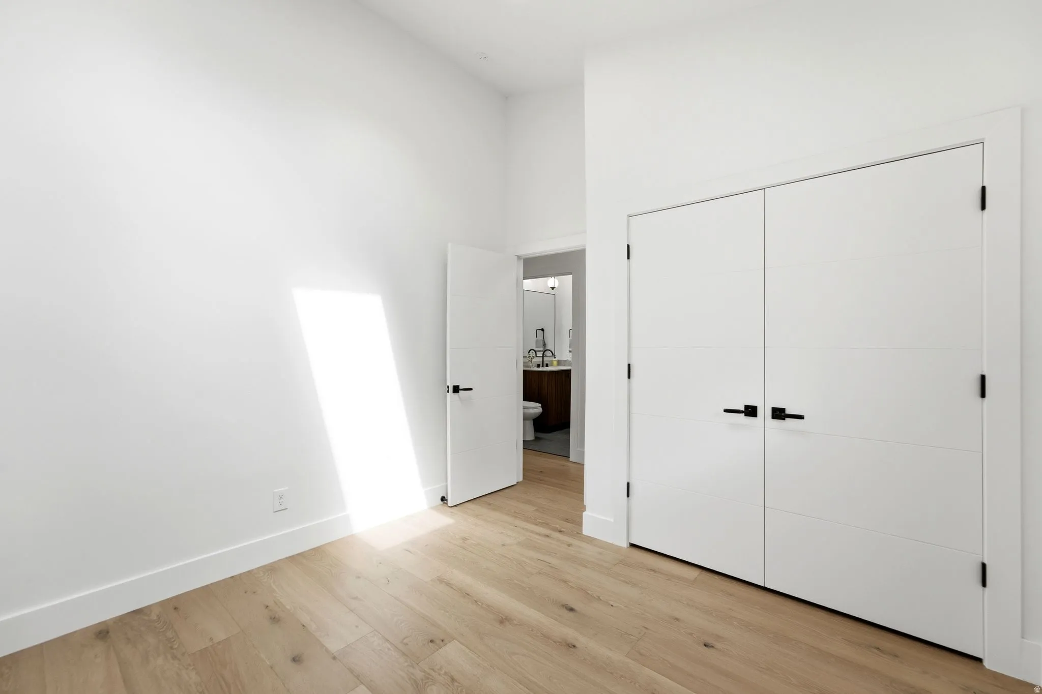 Light wood-finish flooring, white walls, and modern white doors with matte black hardware