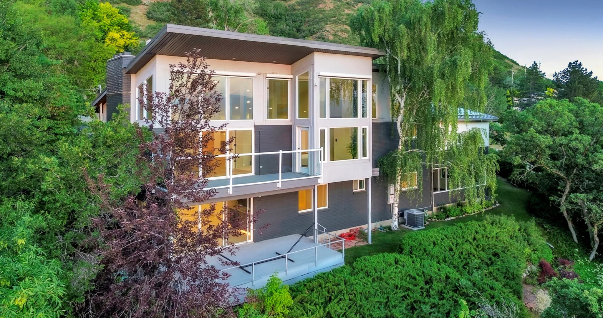 Multi-level architectural design featuring expansive window walls, two exterior balconies with glass railings, a flat roofline, and a stucco and panel exterior