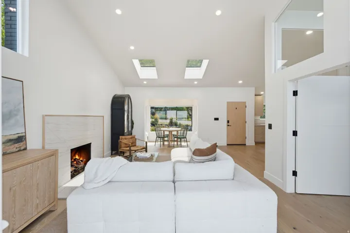 Vaulted ceilings with recessed lighting, two skylights, a fireplace with a stone surround, and wood-finish flooring throughout