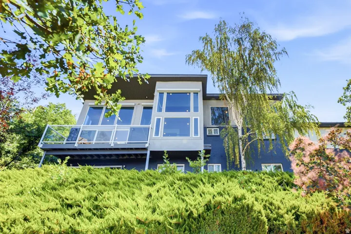 Modern facade with a flat roofline, expansive windows, a glass-paneled deck, and established landscaping